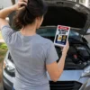 Blinker Fluid Prank Gift Young woman holding a Blinker Fluid prank gift beside a car with the hood open