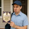 Delivery worker holding a “World’s Smallest Penis Award” prank certificate with a confused expression at a front door.