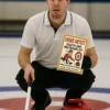 Man posing on a curling rink holding a prank product label