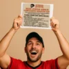 Excited dad holding a funny goalie-themed prank label, celebrating with both hands up.