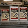 Muffler Bearings Replacement Kit prank displayed as a DIY sticker label, a 6 × 9 bubble mailer and a 6 × 9 mailing box on a vintage auto parts counter.