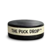 Real hockey puck wrapped with handwritten tape reading “The Puck Drop™”, isolated on a transparent background.