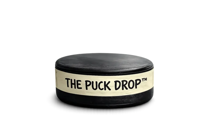 Real hockey puck wrapped with handwritten tape reading “The Puck Drop™”, isolated on a transparent background.