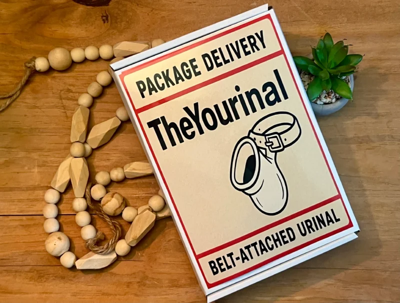 A white prank shipping box for "The Yourinal Belt-Attached Urinal" featuring a humorous illustration of the product, placed on a wooden table next to decorative beads and a succulent.