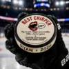 Best Chirper hockey puck award with custom name and year message held by a hockey player on the ice.