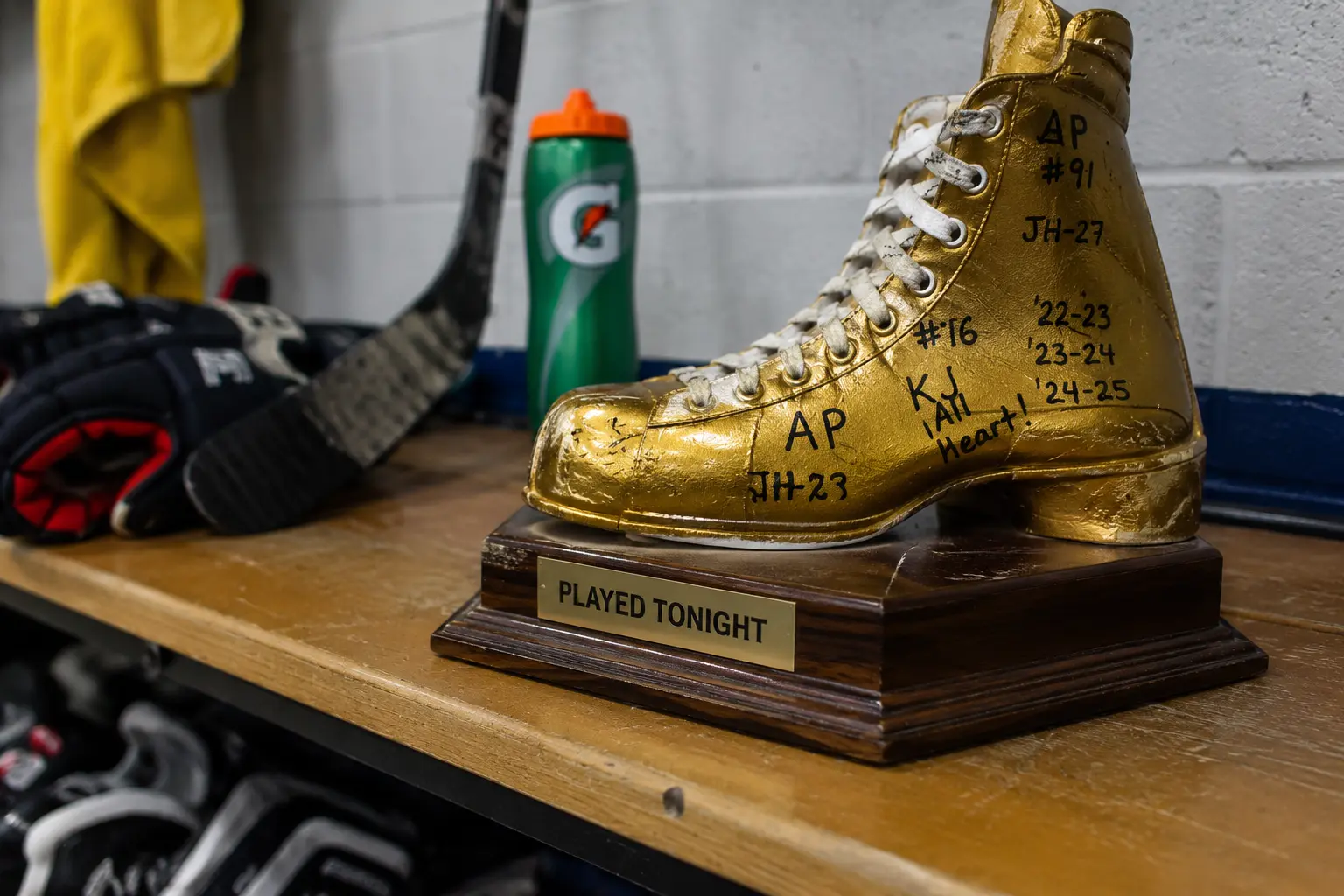 Gold hockey skate traveling trophy on a locker room bench with signatures and season markings.