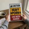 Person holding a Caution Heavy Porn Use Both Hands prank mailer at home