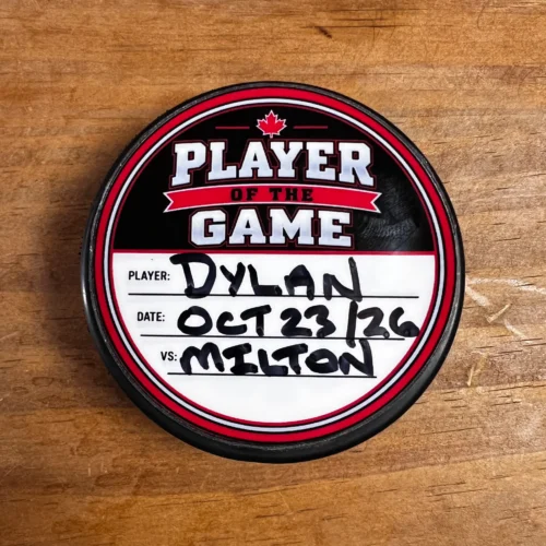 Player of the Game sticker on a black hockey puck, handwritten with Dylan, October 23, 2026, and Milton in the player, date and opponent fields.