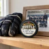 Heart & Hustle Hockey Award Keepsake Hockey puck with a personalized Heart & Hustle sticker displayed beside a worn hockey glove and framed team photo.