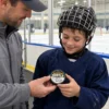 Heart & Hustle Hockey Award - Coach and Player Coach presenting a young hockey player with a puck featuring a personalized Heart & Hustle award sticker at a rink.