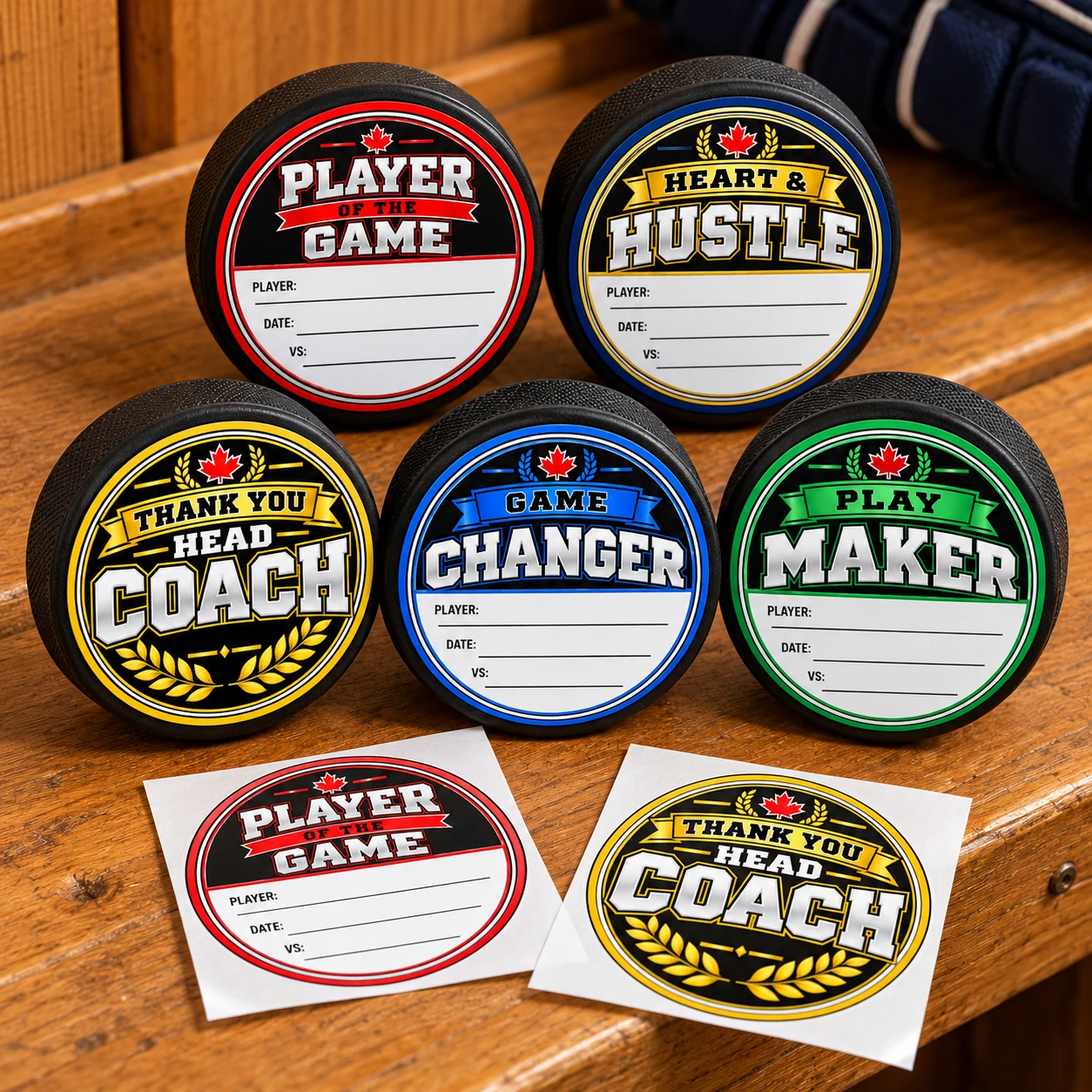 Hockey award and coach thank-you stickers displayed on five black pucks, with two loose stickers on a wooden bench.