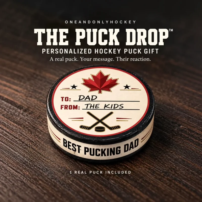 The Puck Drop Personalized Hockey Puck Gift Personalized hockey puck with a Canadian maple leaf, “To: Dad, From: The Kids” on top and “Best Pucking Dad” around the edge, displayed on dark wood.